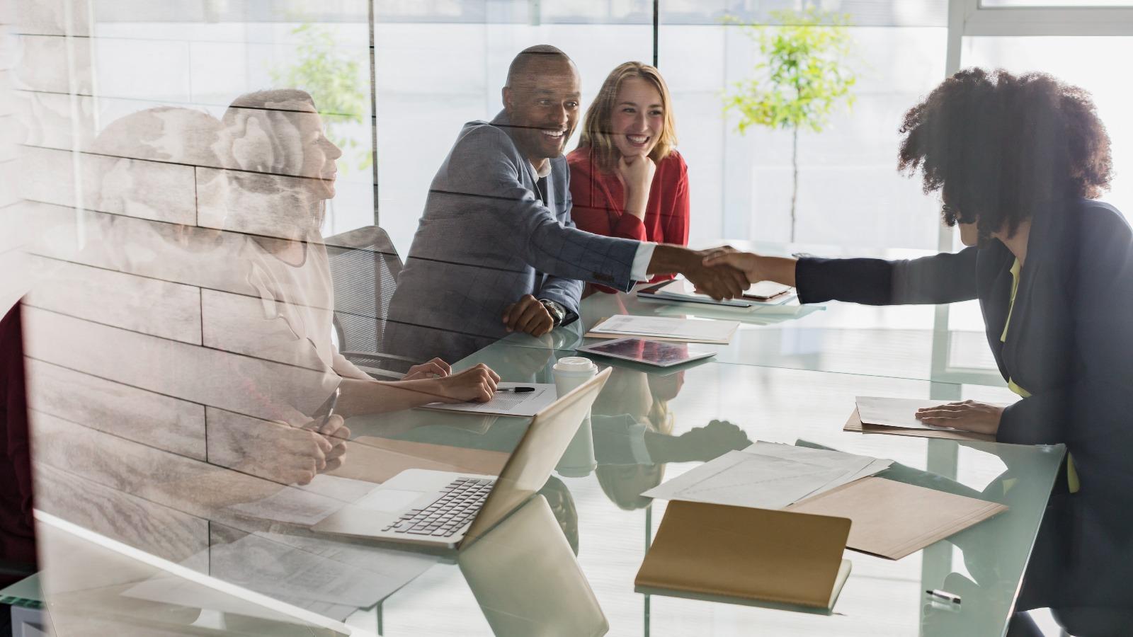 Businessmann und Businessfrau schütteln sich über Konferenztisch die Hände