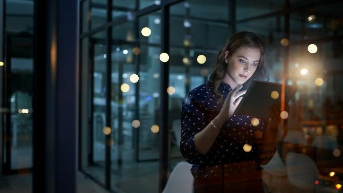 Junge Frau arbeitet spät abends im Büro am Tablet