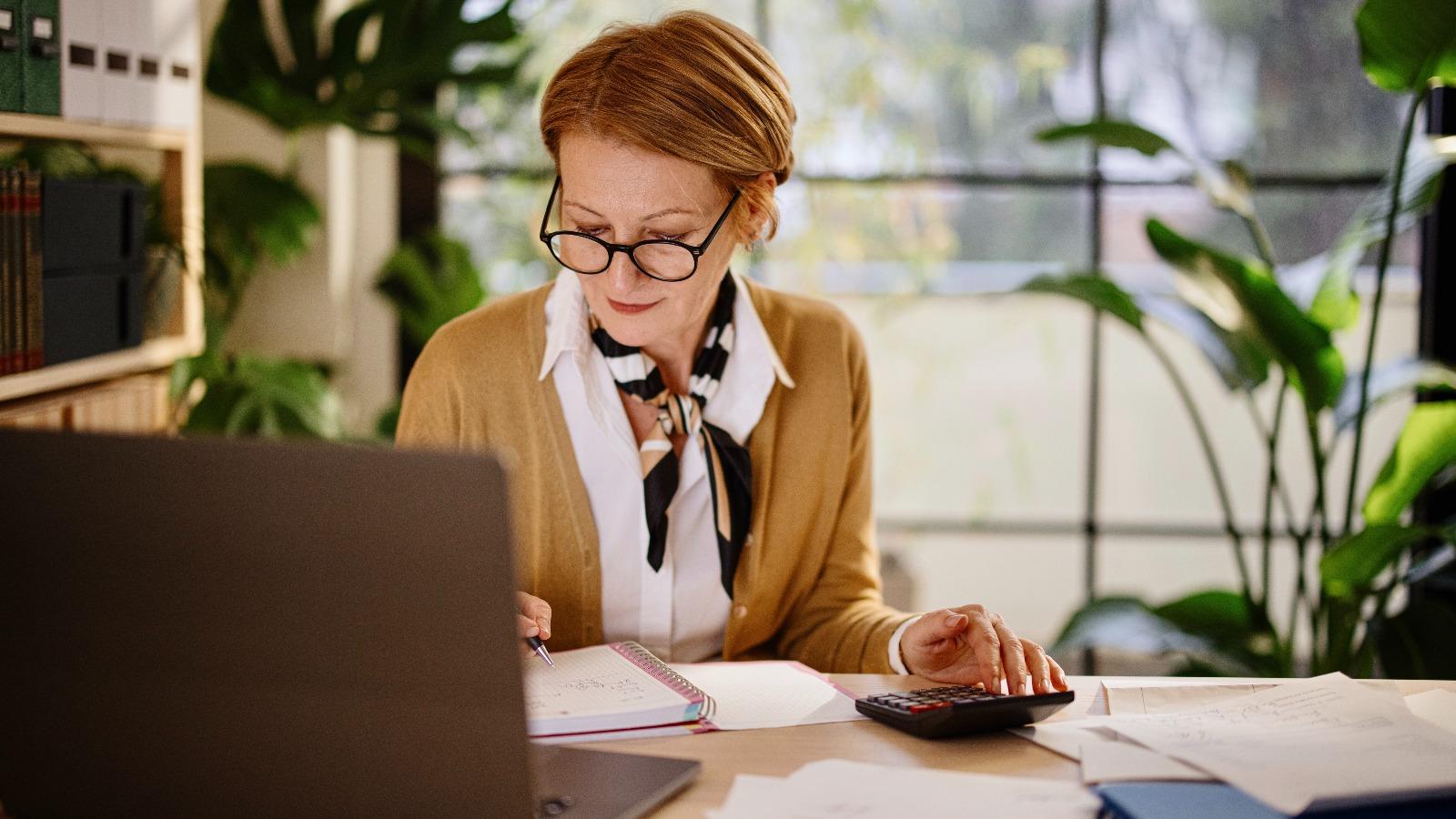 Frau mit Notizbuch und Taschenrechner an Laptop