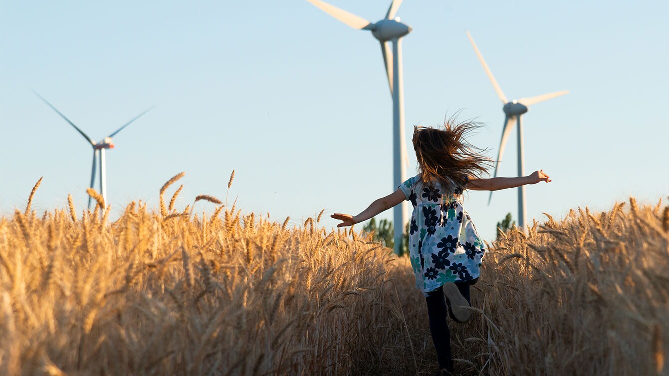 Mädchen rennt durch Getreidefeld vor Windrädern