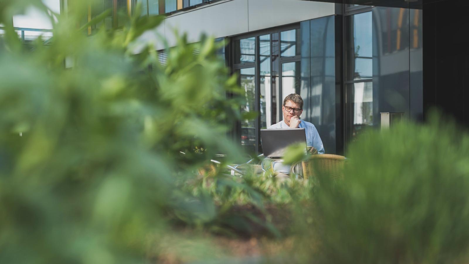 Mann am Laptop zwischen Pflanzen auf Büroterasse