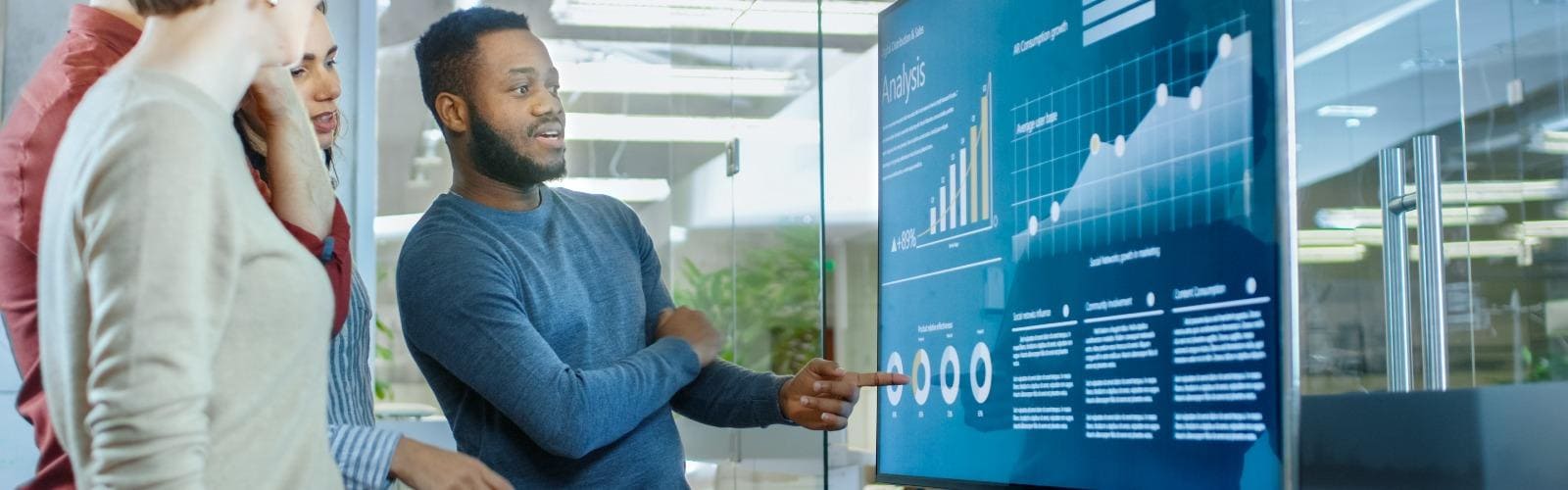 Mann erklärt Kolleginnen Datenanalyse an Screen