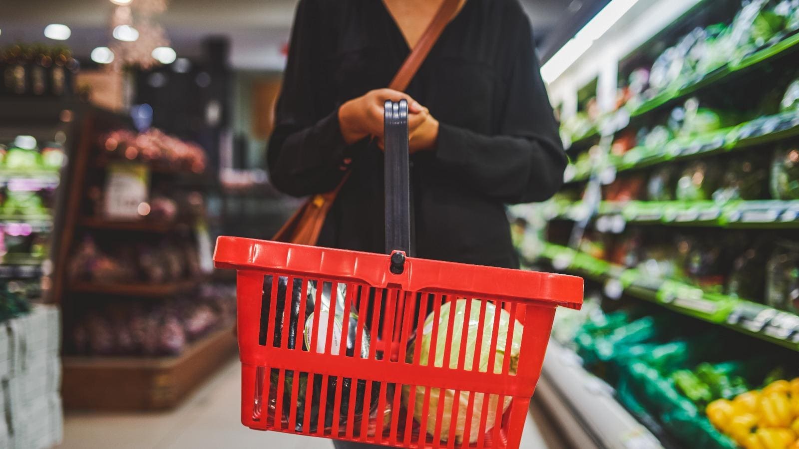 Person mit rotem Einkaufskorb in Supermarkt
